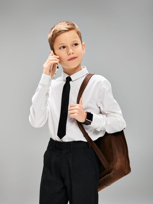 Preadolescent boy in white shirt and tie against gray backdrop, exuding elegance and charm.